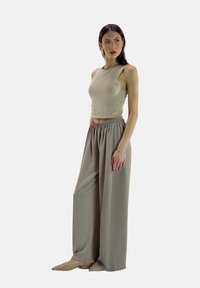 Beige crop top met een mouwloos ontwerp, gecombineerd met lichtbruine, wijde broek met een elastische tailleband. Beide kledingstukken hebben een gladde textuur.