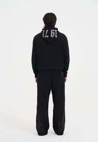 Sudadera negra con capucha y un gran gráfico en la parte posterior, y pantalones de chándal negros a juego con un patrón lineal en el dobladillo.