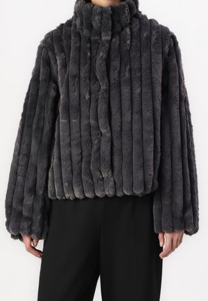Personne portant une veste en fausse fourrure gris foncé à côtes verticales, manches longues et col montant, associée à un pantalon noir.