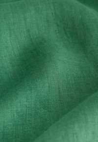 Tissu vert à la texture lisse, présentant un motif de tissage subtil et une couleur uniforme. Le matériau semble léger et doux.