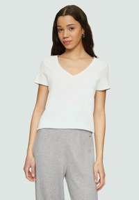 T-shirt en coton blanc avec un col en V et des manches courtes, associé à un pantalon gris à motifs. Texture douce et coupe décontractée.