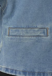 Τζιν ύφασμα με οριζόντια τσέπη με σχισμή, διακοσμημένη με καφέ ραφές και ορατή ραφή κοντά στο κάτω άκρο.