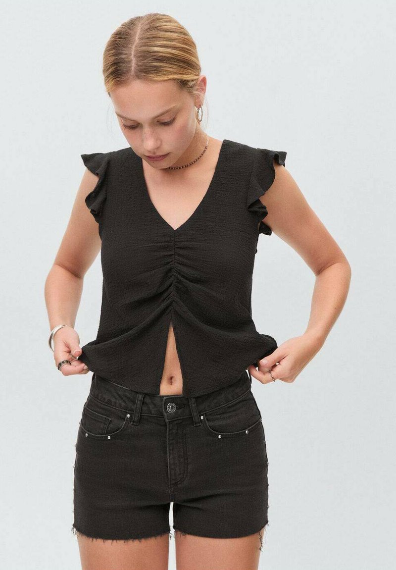 Top nero a maniche corte con scollo a V e dettagli in pizzo, caratterizzato da arricciature frontali e una piccola apertura. Abbinato a pantaloni corti in denim neri.