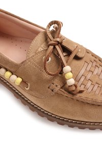 Mocassin en daim marron clair avec un détail en cuir tressé, lacet en cuir noué en forme de nœud et perles en bois sur le côté et aux extrémités des lacets.