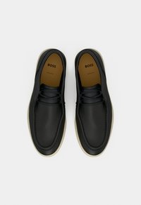 Μαύρα δερμάτινα παπούτσια με υφή, στρογγυλή μύτη και μπεζ καουτσούκ σόλα. Διαθέτουν σχέδιο με κορδόνια και επώνυμη εσωτερική σόλα.