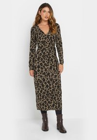 Valkopilkullinen kietaisumekko beigen ja ruskean sävyissä, pitkät hihat, V-pääntie, solmittava vyötärö, polvipituinen, yhdistetty ruskeiden nilkkasaappaiden kanssa. Silkinen pinta.