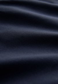 Tessuto blu navy, texture liscia con una lucentezza sottile, caratterizzato da morbide pieghe e leggere ondulazioni, che indicano un materiale di peso medio.