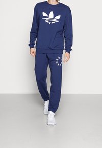 Granatowa bluza z białym logo Adidas oraz pasujące granatowe spodnie z subtelnymi białymi wzorami kwiatowymi, do kompletu białe trampki.