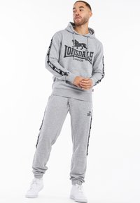 Grauer Kapuzenpullover mit Logo, passende graue Jogginghosen mit seitlichen Streifen. Aus weichem Material, mit elastischen Bündchen und Kordelzügen für einen engen Sitz.