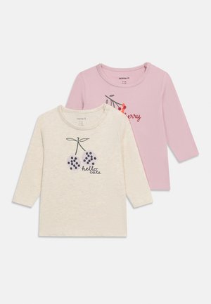 Dos camisetas de manga larga para bebés, una beige con un diseño de cereza morada y el texto "hola lindo", y otra rosa con un diseño de cereza roja y el texto "cereza".