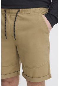 Khaki shorts gjorda av ett mjukt, stretchigt tyg med dragsko i midjan. De har uppvikt fåll och sidofickor.
