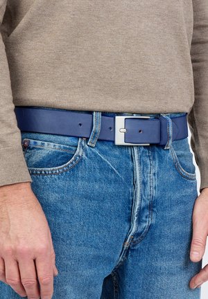 Ceinture en cuir bleu marine avec une boucle rectangulaire en argent, portée sur un jean bleu clair. Surface texturée et détails de couture visibles.