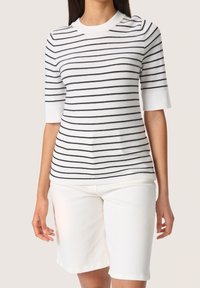 Suéter corto de manga corta blanco con rayas azul marino, que presenta un cuello acanalado y mangas con puños, combinado con pantalones cortos de mezclilla blancos.