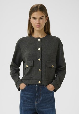 Dunkelgraue, cropped Jacke mit rundem Ausschnitt, vorderem Knopfverschluss, zwei Taschen und goldfarbenen Hardware-Akzenten. Über blauen Jeans getragen.