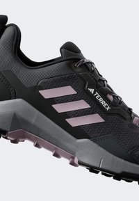 Svart och grå atletisk sko med en strukturerad ovandel, rosa detaljer, tre-stripes logotyp och en robust sula för grepp.