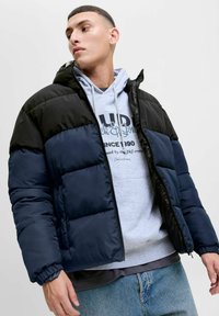 Puffervest med et farveblokdesign i sort og marineblå, med hætte, elastiske manchetter og lynlås. Teksturstof med en blank overflade.