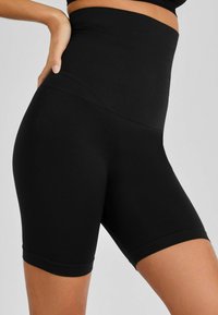 Shorts neri a vita alta realizzati in un tessuto elasticizzato, caratterizzati da una texture liscia e una silhouette aderente, che terminano a metà coscia con orlo senza cuciture.