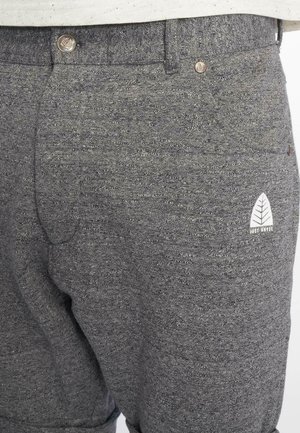 Gray sweatpants featuring a textured fabric, elasticated waistband, and a small white logo design on the side. Two front pockets visible.