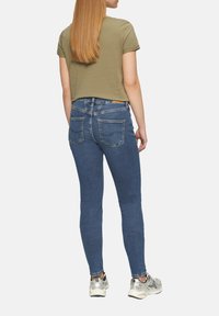 T-shirt en coton vert associé à un jean skinny bleu foncé. Le jean présente un design classique avec cinq poches et une légère élasticité.