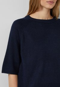 Marineblauwe gebreide trui met een ronde hals, korte mouwen en een zachte textuur. Heeft een ontspannen pasvorm en is voorzien van raglanmouwen.