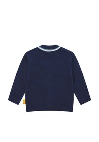 Marineblauwe trui met lange mouwen, ronde hals en lichtblauwe biezen. Gemaakt van zachte knitstof met een gele tag aan de zijkant.