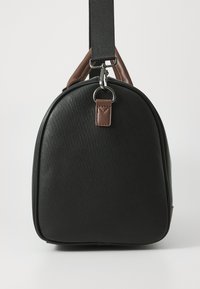 Bolso sintético negro texturizado con parte superior redondeada, acentos de cuero marrón y una correa removible. Presenta un accesorio de hardware plateado.