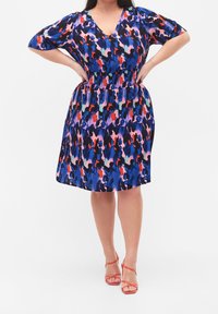 Kukallinen mekko, jossa on V-pääntie, lyhyet hihat ja joustava vyötärö. Väreinä sininen, violetti, punainen ja vaaleat sävyt.