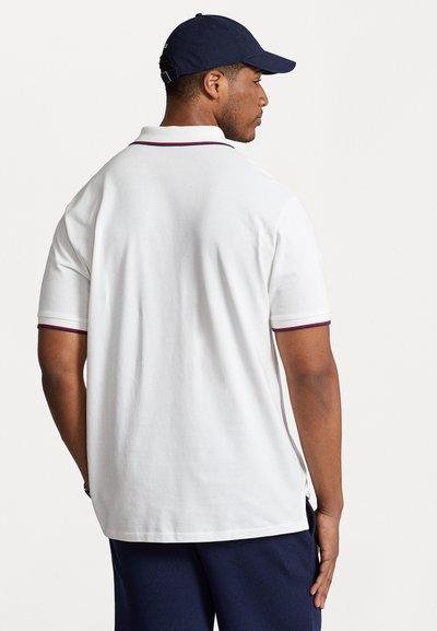 Polo shirt blanc à manches courtes avec un col marine et des détails d'accent rouge, fabriqué en coton. La vue arrière montre des fentes latérales et un tissu texturé.