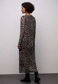 Dlouhé, průhledné šaty s leopardím potiskem vyrobené z lehkého materiálu, s dlouhými rukávy a volným střihem, v kombinaci s černými kotníkovými botami.