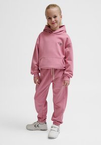 Roze hoodie met een voorzak, vergezeld van bijpassende joggingsbroek. Bevat elastische manchetten en een trekkoord bij de taille. Sportieve sneakers.
