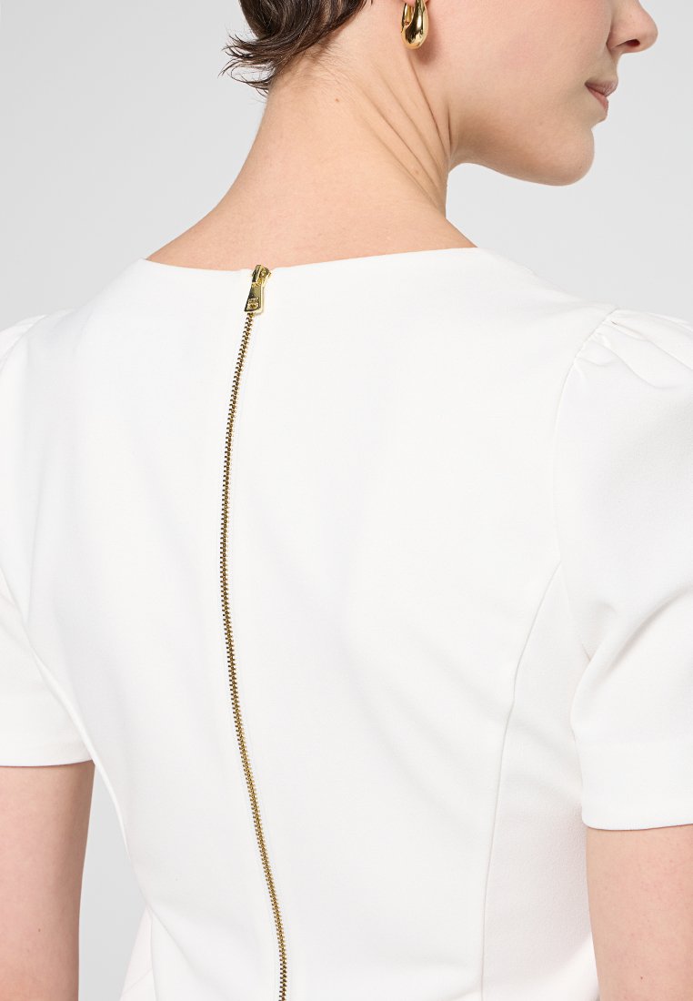 Biała sukienka z wyraźnym złotym zamkiem błyskawicznym z tyłu, krótkimi rękawami i gładkim, usztywnionym materiałem.