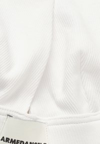 Gros plan d'un vêtement en tissu côtelé blanc avec des coutures visibles et une étiquette partiellement visible.