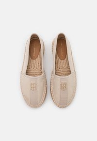 Espadrilles en toile beige avec semelles en jute tissé, présentant une tige texturée, des panneaux latéraux élastiques ton sur ton et un détail de logo métallique.