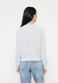 Ljusgrå tröja med ribbat nederdel och ärmslut, med en rundad halsringning. Matchas med högmidjade blå denimjeans.