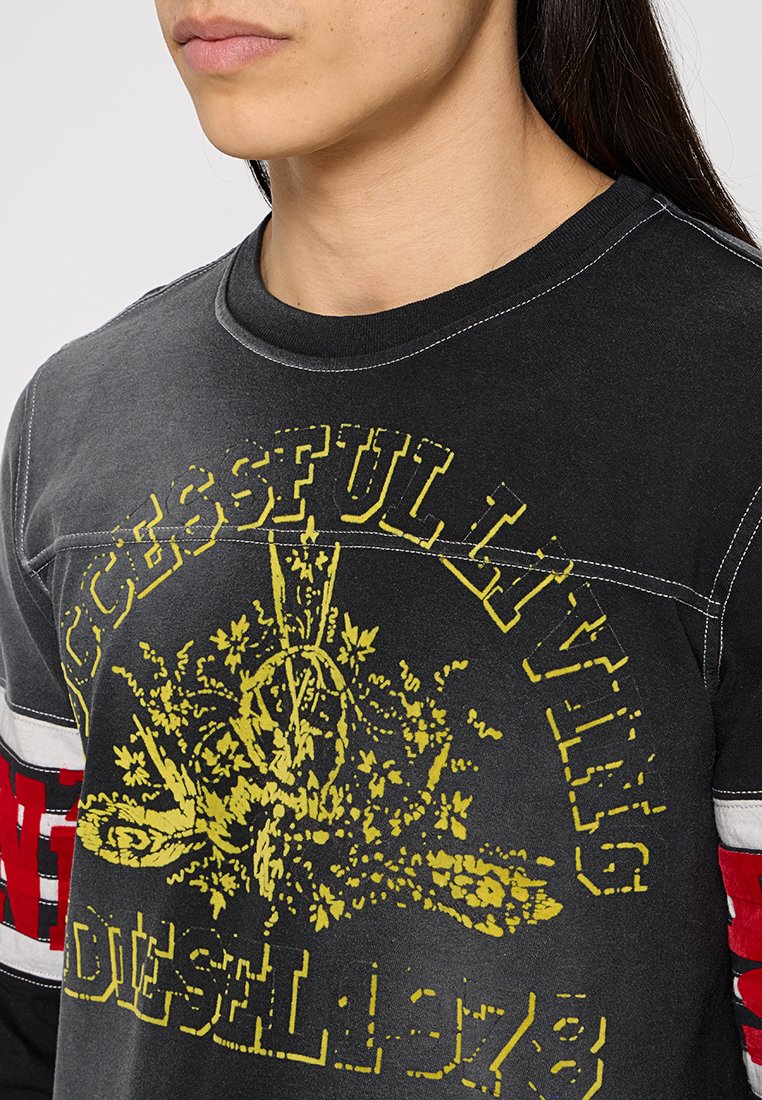 Schwarzes Langarm-T-Shirt mit gelber Grafik, Text und Design, mit weißen und roten gestreiften Akzenten an den Ärmeln. Weicher Stoff.