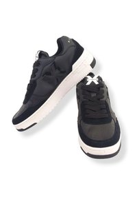 Un paio di sneakers nere a bassa altezza con suole bianche, lacci neri e un logo "X" testurizzato sul lato e sulla linguetta, esposte su uno sfondo bianco.