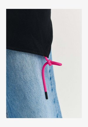 Fekete póló rózsaszín zsinórral megkötve az alján világoskék farmernadrág felett, egyszerű háttér előtt.