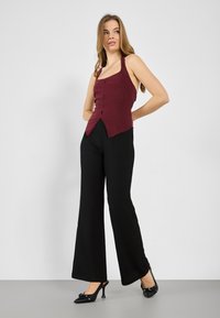 Burgundy halter top with front button closure, paired with black wide-leg trousers and black high-heeled shoes. Smooth fabric and tailored fit.