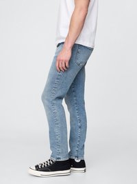 Vaqueros de denim en azul claro con corte ajustado, que presentan un efecto de lavado desgastado, diseño de cinco bolsillos y combinados con zapatillas altas negras.