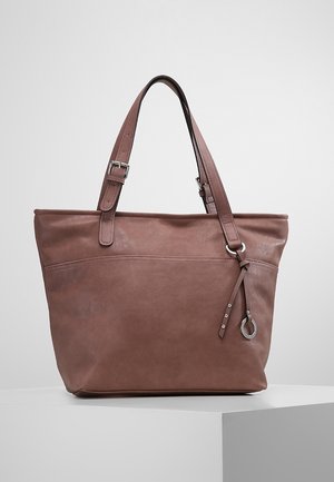 Bolso tote de cuero marrón con correas ajustables para el hombro y un pequeño colgante de anillo metálico en un lado, exhibido sobre un pedestal blanco.