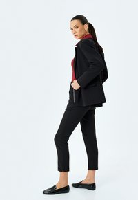 Blazer noir par-dessus un haut rouge, associé à un pantalon noir fuselé et des mocassins. Présente un design ajusté, un tissu lisse et des détails subtils.