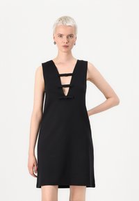 Čierne šaty bez rukávov s hlbokým výstrihom do V, ktoré majú tri čierne mašle. Hladký materiál s elegantným a jednoduchým strihom.