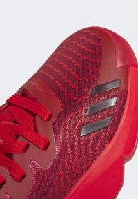 Zapatilla deportiva roja con un upper de punto texturizado, cordones gruesos y acentos metálicos oscuros en los laterales. Suela curva para un mayor soporte.