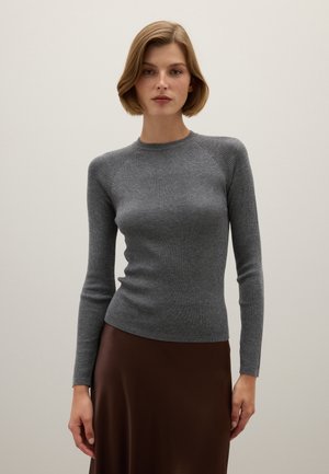 Grauer gerippter Strickpullover mit langen Ärmeln und rundem Ausschnitt, getragen mit einem braunen seidigen Rock. Sanfte Textur und taillierte Passform.