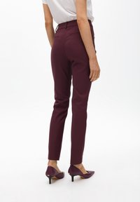 Pantalones ajustados burdeos con una textura suave, corte entallado y bolsillos traseros estándar. Combinados con tacones de punta.