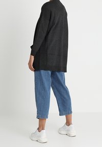Charcoal gray oversized cardigan with wide sleeves, paired with light blue cropped jeans and white sneakers, shown from the back.