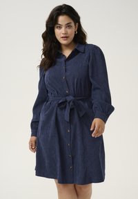 Tumedatees särgidress, mis on valmistatud tekstuurigast kangast, nööpidega ees, pikkade varrukatega ja seotud vöödetailiga. Minimalistlik disain.