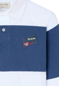 Polo de rayas azul marino y blancas, con una textura suave de algodón, cuello con botones y dos parches triangulares bordados.