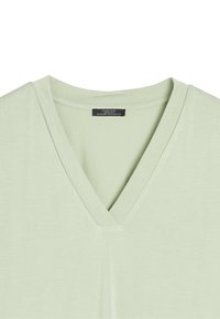 T-shirt z dekoltem w serek w jasnym zielonym kolorze, z miękkiego materiału o gładkiej teksturze. Posiada prosty design i małą metkę marki przy dekolcie.