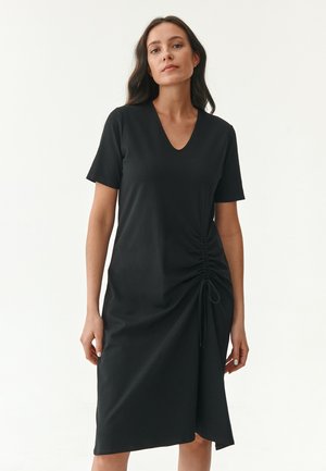 Black dress with a V-neck and short sleeves. Features side ruching with drawstring for adjustable fit. Soft, smooth fabric with a relaxed silhouette.